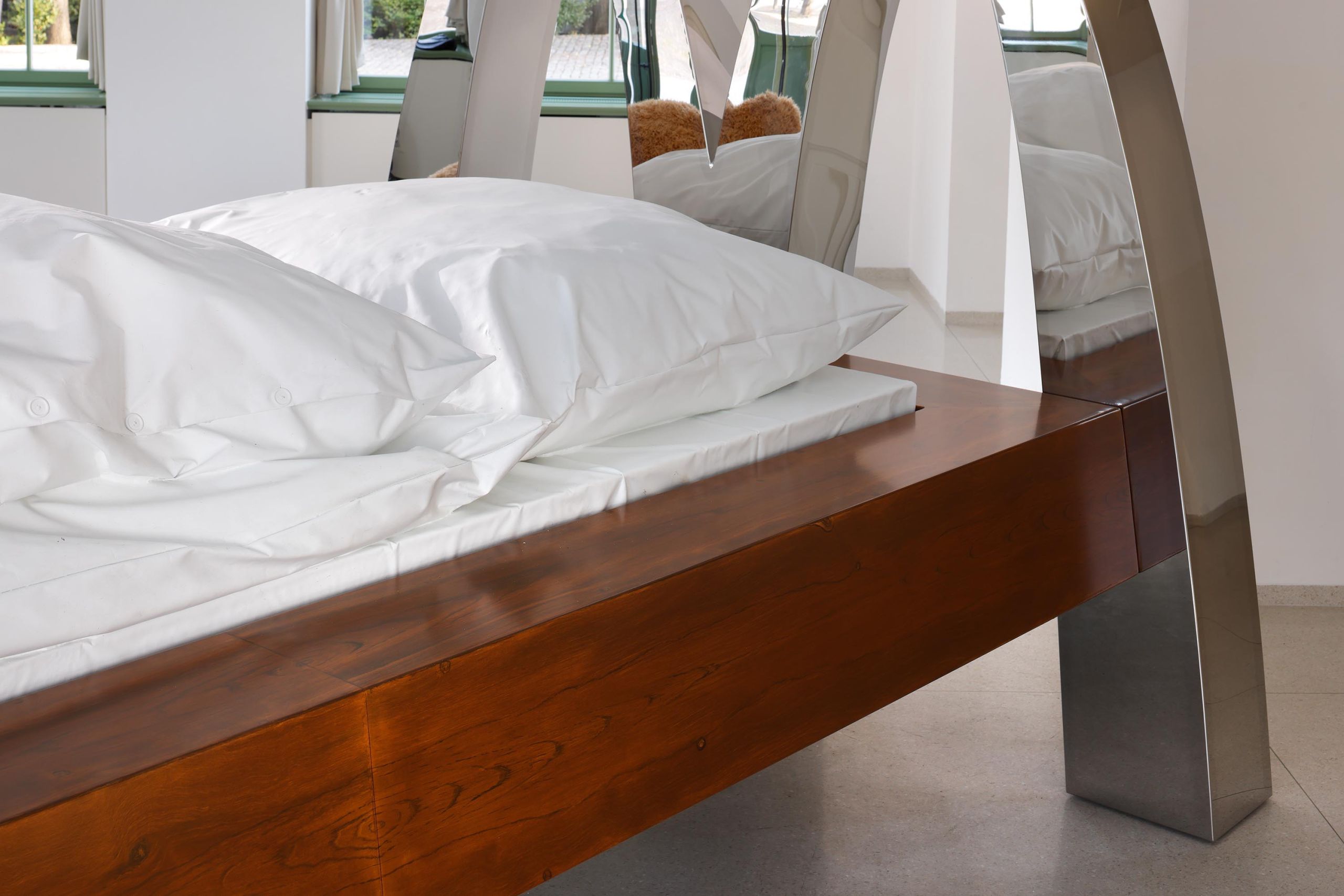 McBed: white bedding on the walnut frame between the chrome arches